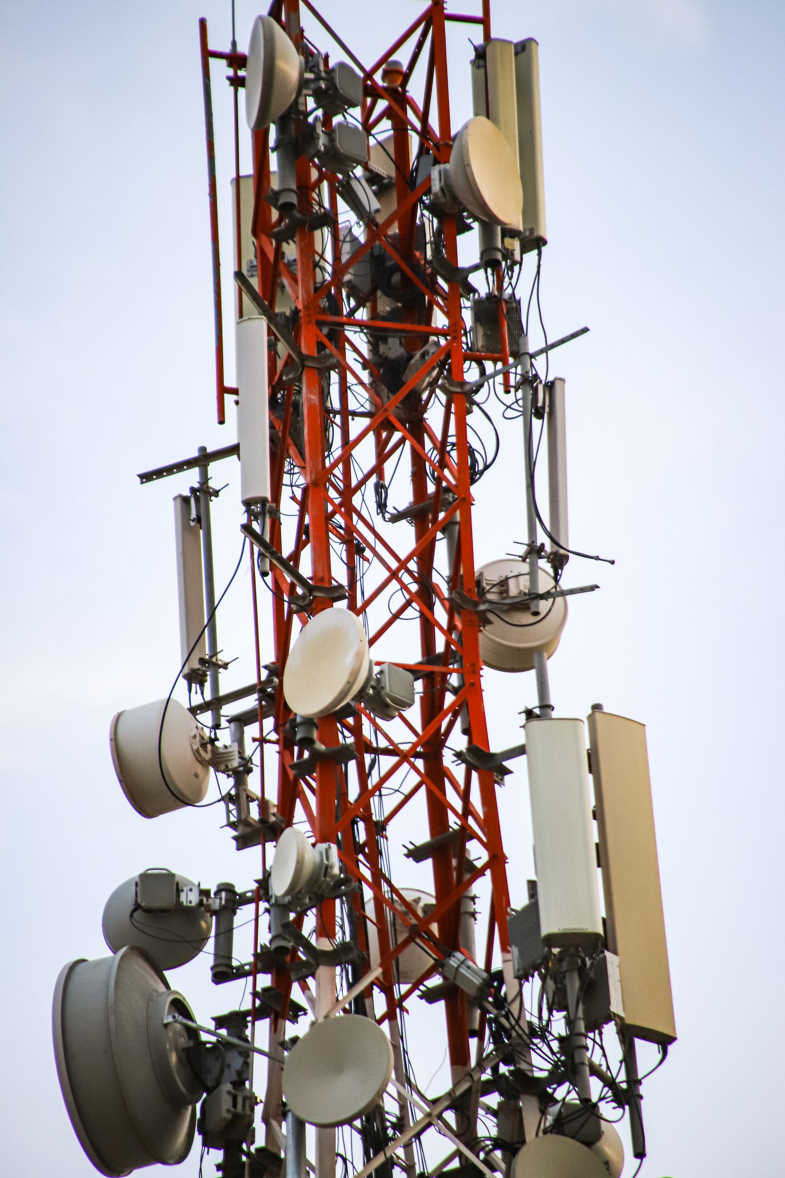 Close da parte superior de uma torre treliçada vermelha coberta de antenas parabólicas e painéis.