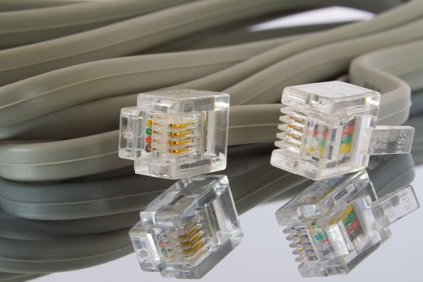 Dois conectores RJ11 transparentes em um cabo chato cinza, com reflexo.